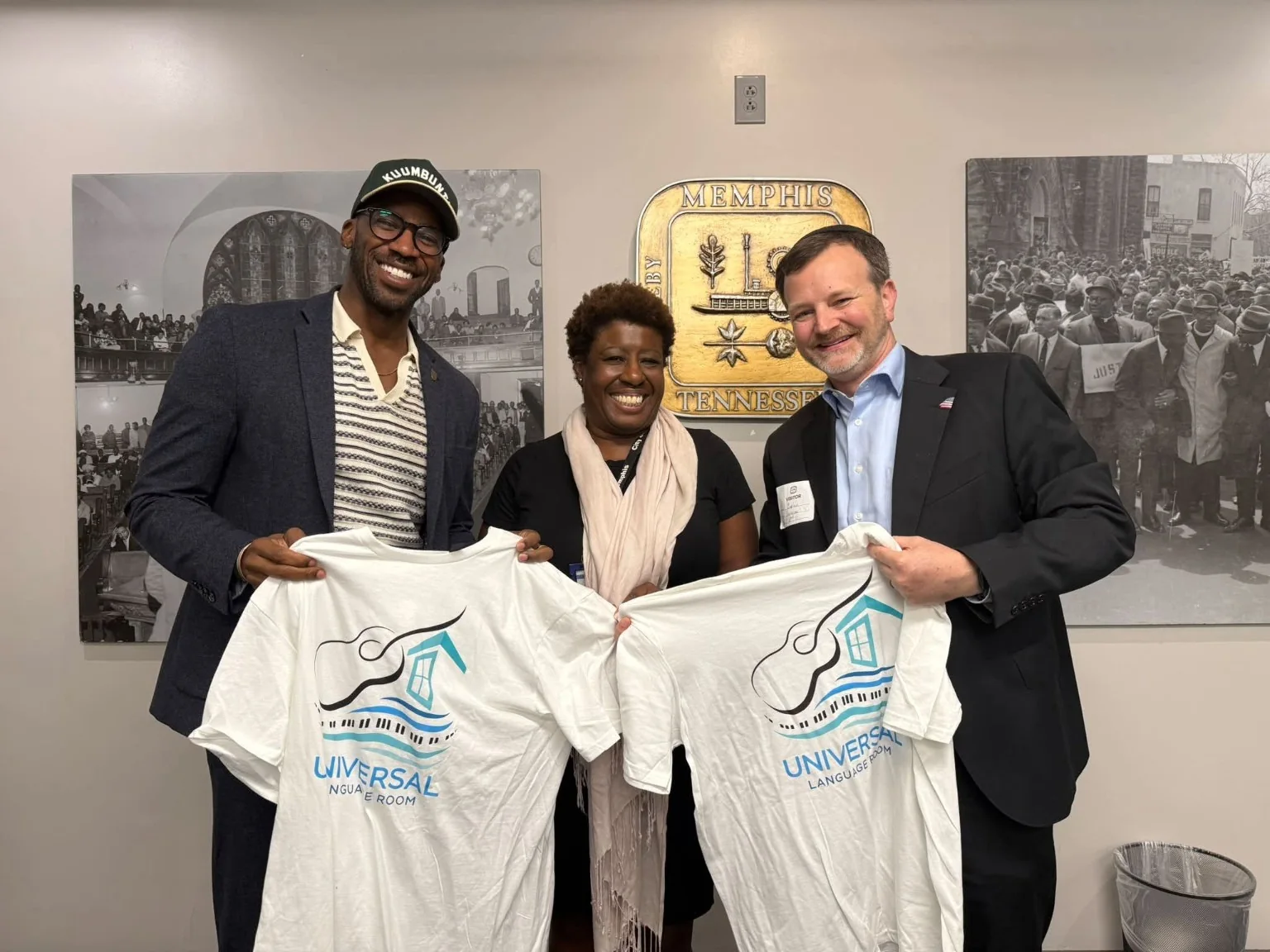 Three community participants holding Universal Language Room shirts in a Memphis civic setting.