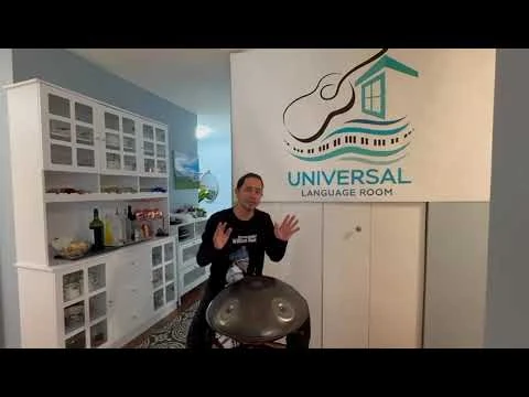 A Universal Language Room collaborator seated beside a handpan and the program sign.